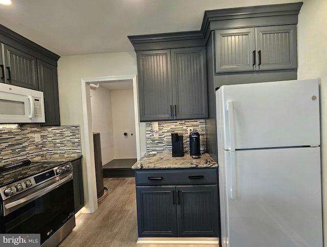 kitchen featuring wood-type flooring, light stone countertops, backsplash, and white appliances