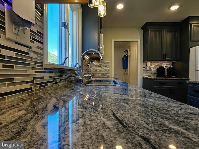 kitchen featuring pendant lighting, sink, backsplash, and dark stone counters