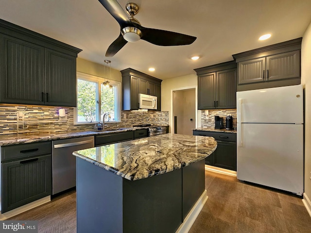 kitchen featuring appliances with stainless steel finishes, a center island, tasteful backsplash, light stone counters, and decorative light fixtures