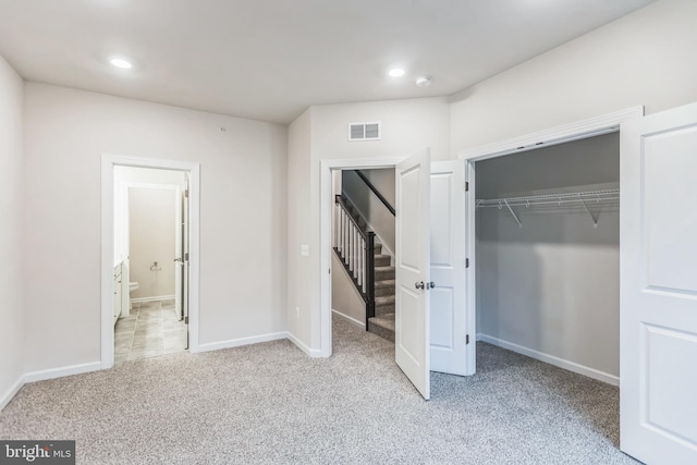 unfurnished bedroom featuring ensuite bath, light colored carpet, and a closet