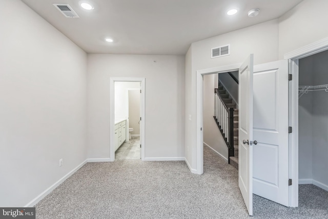 unfurnished bedroom with light colored carpet, a closet, ensuite bath, and a spacious closet