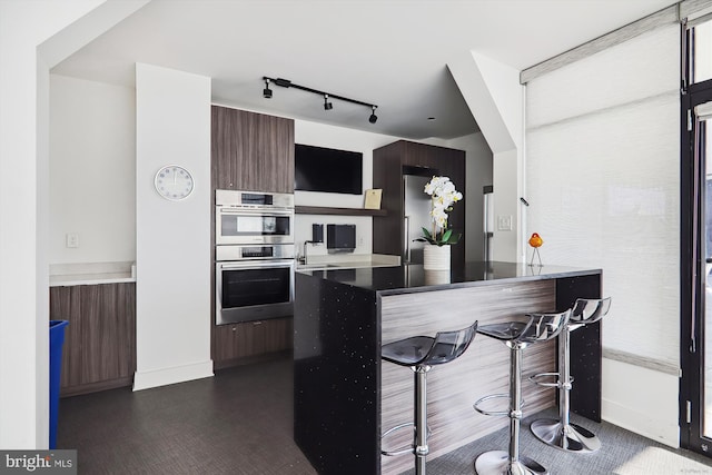 kitchen featuring double oven, kitchen peninsula, dark brown cabinetry, and a breakfast bar area