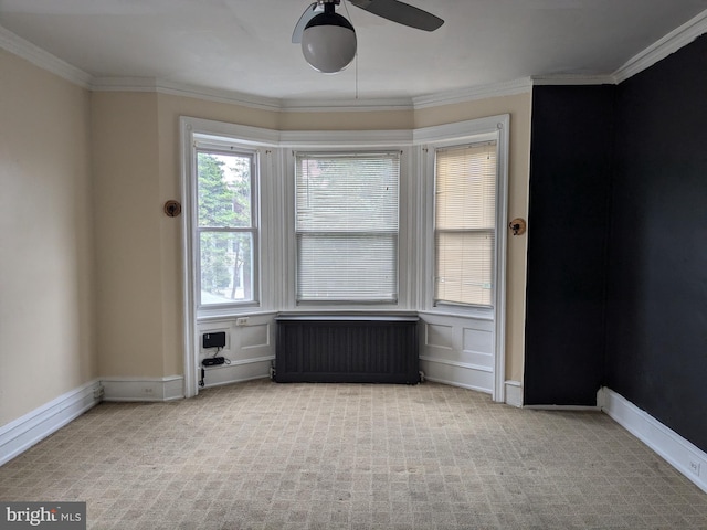 spare room featuring crown molding, ceiling fan, radiator heating unit, and light carpet