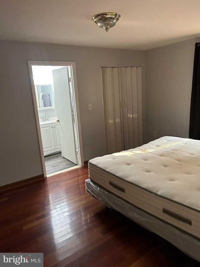 bedroom with ensuite bathroom, sink, and dark wood-type flooring