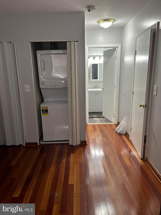 corridor with stacked washer and dryer, sink, and dark wood-type flooring