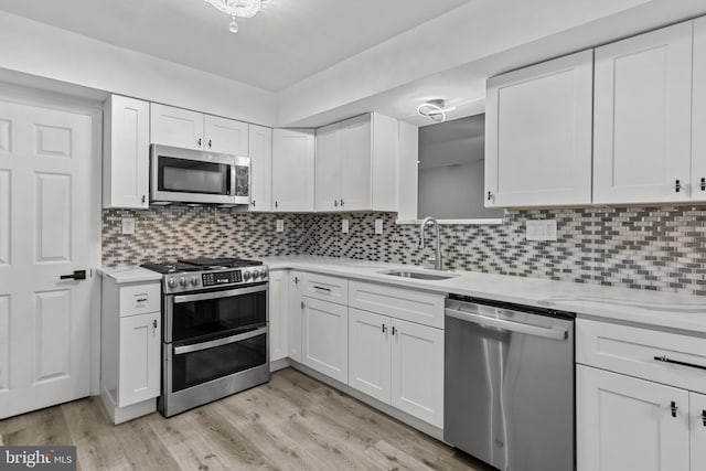 kitchen featuring stainless steel appliances, white cabinetry, light hardwood / wood-style floors, and sink