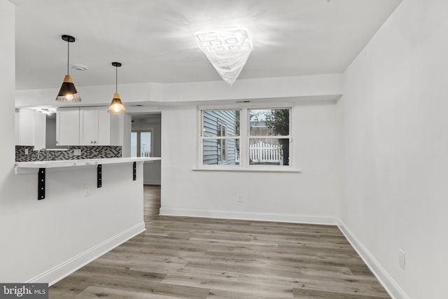 kitchen featuring white cabinets, hanging light fixtures, a kitchen breakfast bar, light hardwood / wood-style flooring, and backsplash