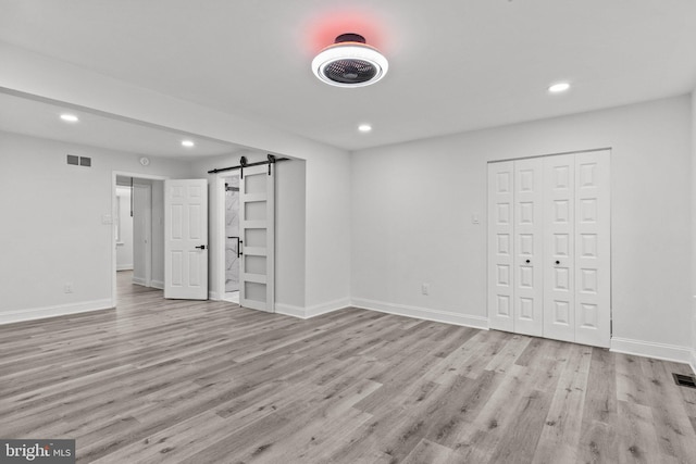 unfurnished bedroom with a barn door and light hardwood / wood-style floors