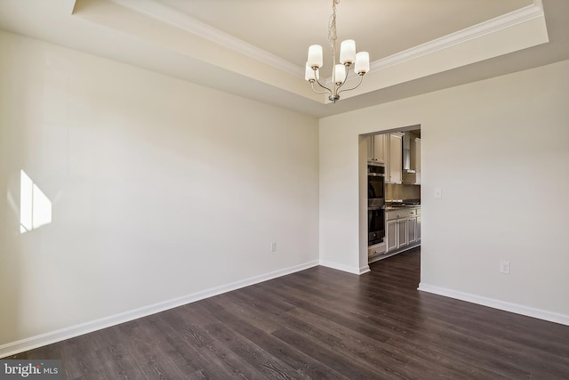 empty room with an inviting chandelier, a raised ceiling, ornamental molding, and dark hardwood / wood-style flooring