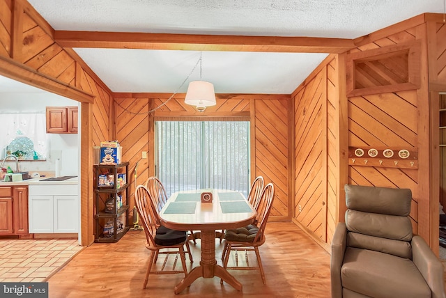 dining room featuring beam ceiling, wood walls, a textured ceiling, and sink