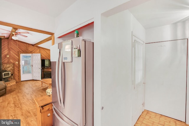 kitchen with ceiling fan, stainless steel refrigerator, vaulted ceiling with beams, a wood stove, and wooden walls