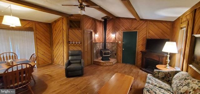 living room featuring light hardwood / wood-style floors, a wood stove, wood walls, and vaulted ceiling with beams