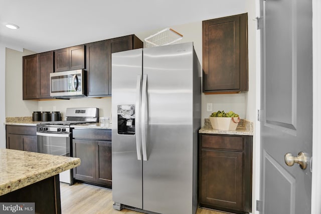 kitchen featuring light hardwood / wood-style flooring, dark brown cabinets, appliances with stainless steel finishes, and light stone countertops