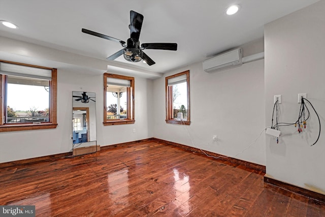 empty room with a healthy amount of sunlight, a wall mounted AC, dark wood-type flooring, and ceiling fan