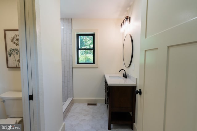 bathroom featuring tile patterned flooring, a tile shower, vanity, and toilet