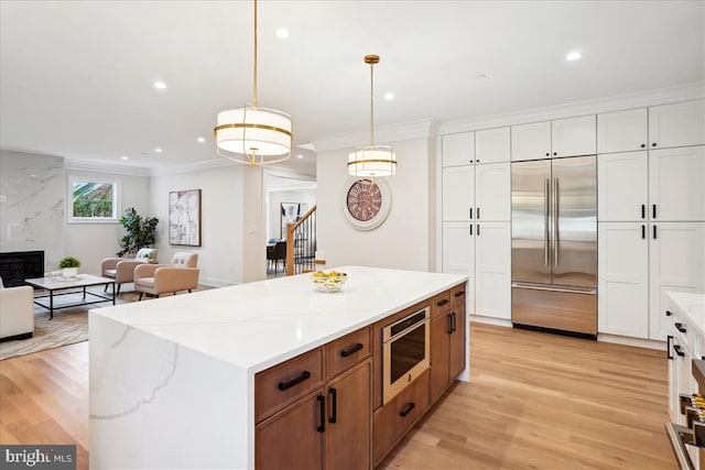 kitchen with appliances with stainless steel finishes, hanging light fixtures, light hardwood / wood-style floors, and white cabinetry