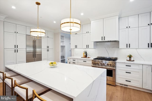 kitchen with light wood-type flooring, white cabinetry, hanging light fixtures, a kitchen island, and high quality appliances