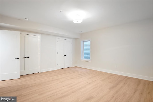 unfurnished bedroom with light hardwood / wood-style floors and multiple closets