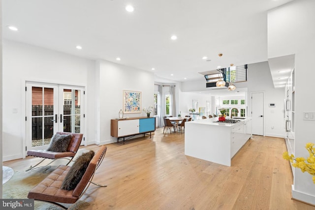 kitchen with a skylight, an island with sink, sink, french doors, and light wood-type flooring