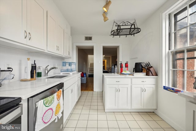 kitchen with light tile patterned floors, sink, stainless steel dishwasher, white cabinetry, and decorative backsplash