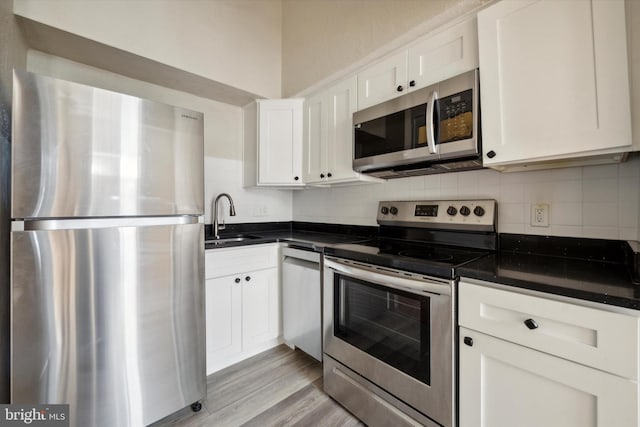 kitchen featuring decorative backsplash, stainless steel appliances, sink, white cabinetry, and light hardwood / wood-style flooring