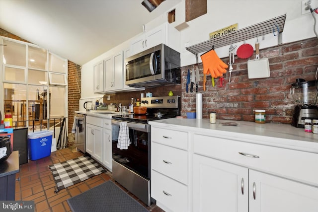 kitchen with lofted ceiling, sink, brick wall, white cabinetry, and stainless steel appliances