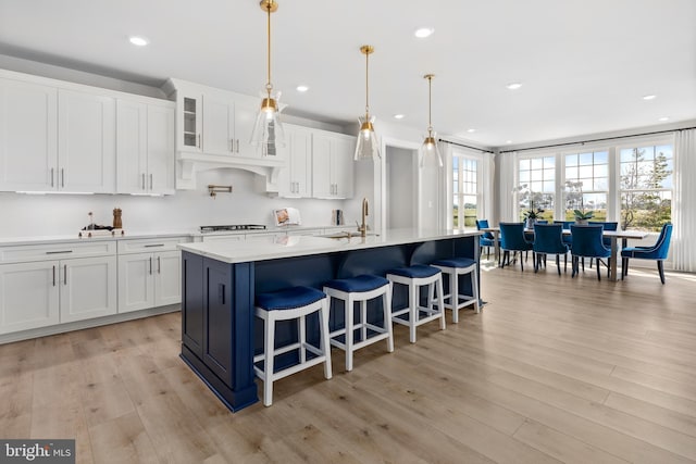 kitchen with a center island with sink, hanging light fixtures, light hardwood / wood-style floors, and white cabinetry