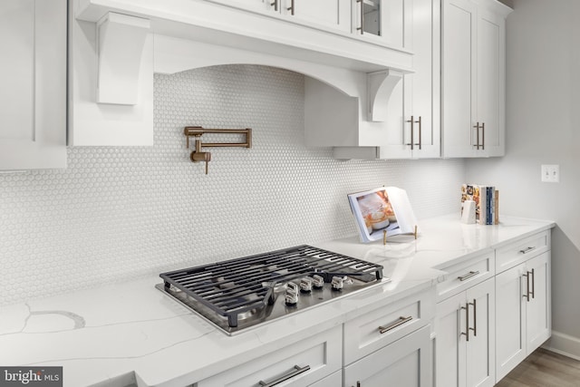 kitchen with stainless steel gas stovetop, white cabinets, light stone counters, and light hardwood / wood-style floors