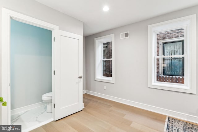 unfurnished bedroom featuring ensuite bath, multiple windows, and light hardwood / wood-style flooring