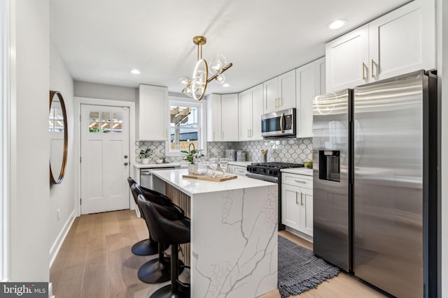 kitchen featuring pendant lighting, white cabinets, light hardwood / wood-style flooring, and stainless steel appliances