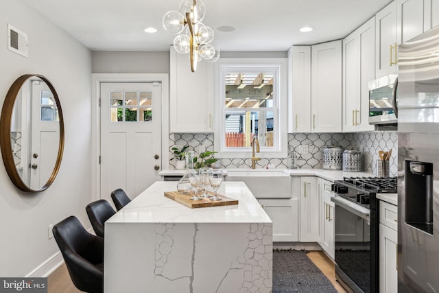 kitchen with white cabinets, a kitchen bar, stainless steel appliances, and decorative light fixtures