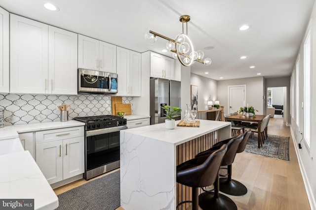 kitchen with appliances with stainless steel finishes, light hardwood / wood-style flooring, pendant lighting, and white cabinetry