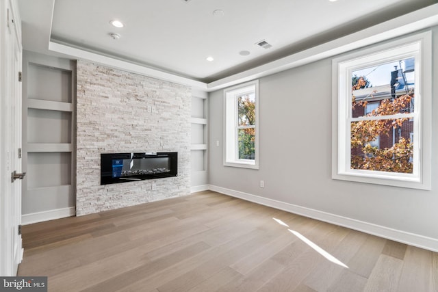 unfurnished living room featuring light hardwood / wood-style floors, a fireplace, and built in shelves