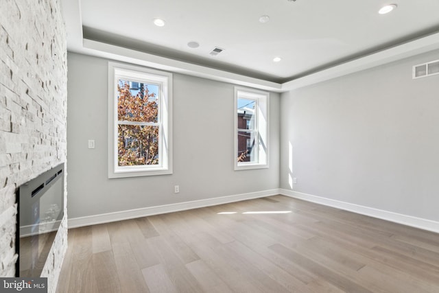 unfurnished living room with light hardwood / wood-style floors, a stone fireplace, a tray ceiling, and a healthy amount of sunlight