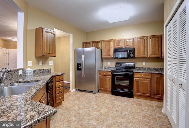 kitchen with light tile patterned flooring, dark stone counters, sink, and black appliances