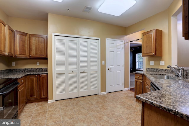 kitchen with dark stone countertops, black electric range, sink, and light tile patterned flooring