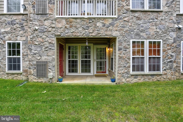 entrance to property with a balcony, a lawn, and central air condition unit