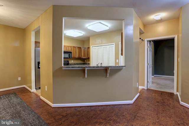 kitchen with stainless steel fridge, kitchen peninsula, a kitchen breakfast bar, dark hardwood / wood-style floors, and light stone countertops