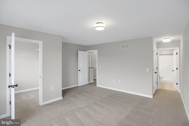 unfurnished bedroom featuring a closet, light colored carpet, a walk in closet, and ensuite bath