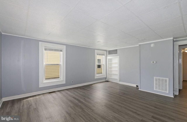 unfurnished room featuring crown molding, a drop ceiling, dark hardwood / wood-style floors, and built in features