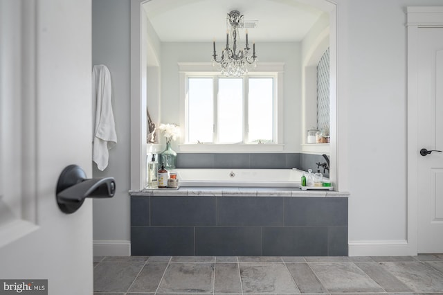 bathroom with a chandelier and tiled tub