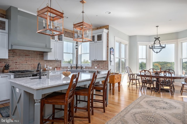 kitchen with a kitchen island with sink, light stone countertops, light wood-type flooring, and backsplash