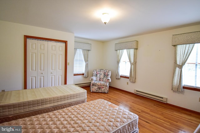 bedroom with multiple windows, hardwood / wood-style floors, a closet, and a baseboard radiator