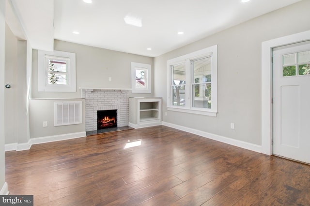 unfurnished living room featuring a brick fireplace, dark hardwood / wood-style flooring, and a healthy amount of sunlight