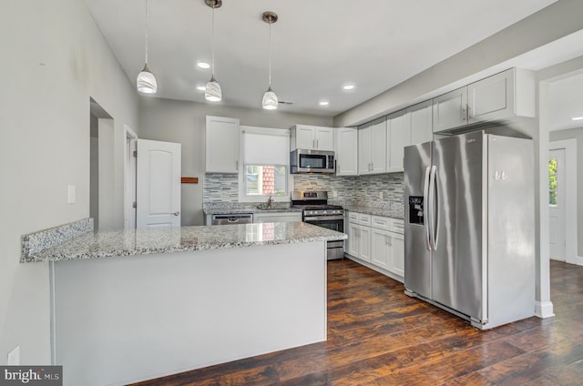 kitchen with white cabinets, kitchen peninsula, decorative light fixtures, dark wood-type flooring, and appliances with stainless steel finishes