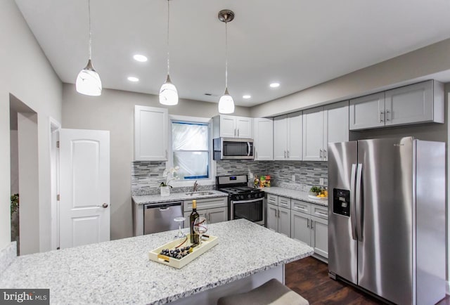 kitchen featuring light stone countertops, dark hardwood / wood-style flooring, hanging light fixtures, a breakfast bar area, and appliances with stainless steel finishes