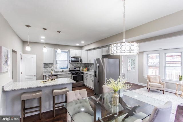 kitchen featuring light stone countertops, decorative backsplash, dark wood-type flooring, hanging light fixtures, and appliances with stainless steel finishes