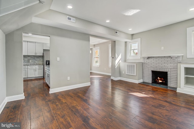 unfurnished living room with a brick fireplace and dark hardwood / wood-style floors