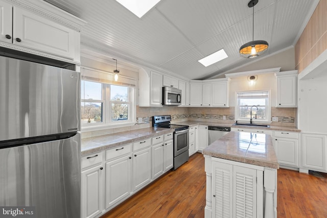 kitchen with appliances with stainless steel finishes, decorative light fixtures, sink, white cabinets, and a center island