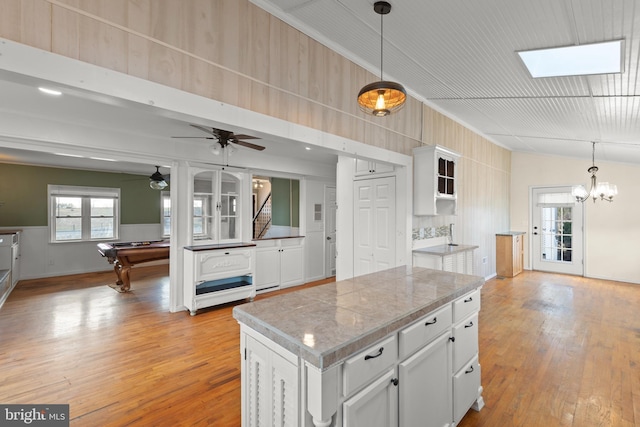 kitchen with hanging light fixtures, light hardwood / wood-style floors, white cabinets, a kitchen island, and ceiling fan with notable chandelier